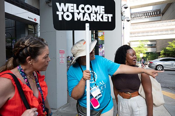 Woman Pointing at Atlanta Market holding a, "Welcome to Market!" sign