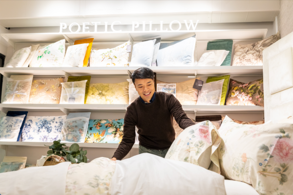 Man fluffing pillows and a bed under Poetic Pillow